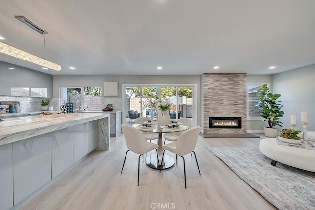 dining area featuring recessed lighting, a tiled fireplace, and light wood-style floors