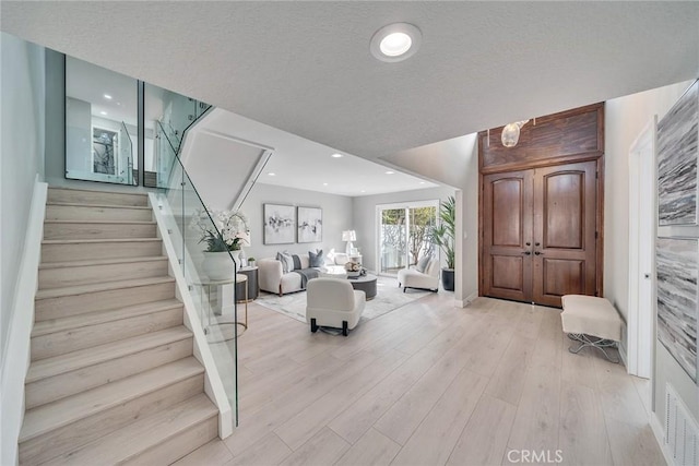 foyer entrance with recessed lighting, stairway, light wood finished floors, and a textured ceiling