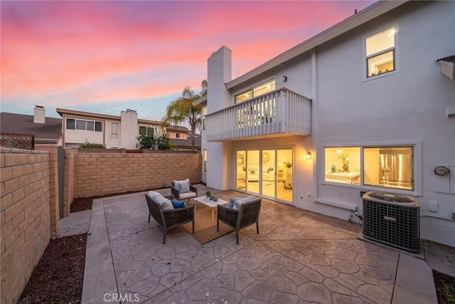 patio terrace at dusk with cooling unit, an outdoor living space, a fenced backyard, and a balcony