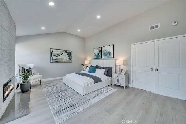 bedroom with lofted ceiling, light wood-style flooring, a fireplace, visible vents, and a closet