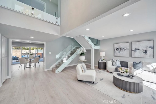 living area with baseboards, a towering ceiling, stairs, light wood-style floors, and recessed lighting