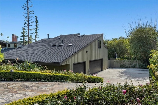 view of side of property featuring a garage, driveway, and a shingled roof