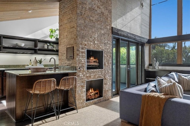 bar with a high ceiling, carpet flooring, a sink, a lit fireplace, and wet bar