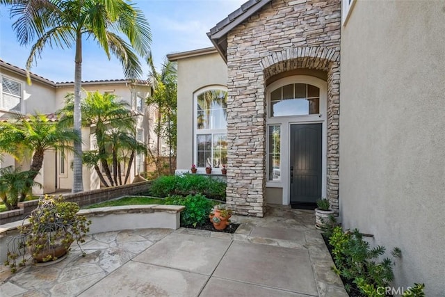 doorway to property with stone siding, a patio area, and stucco siding