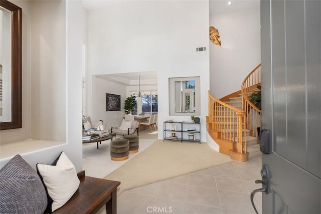 foyer entrance featuring visible vents, a high ceiling, light tile patterned flooring, a chandelier, and stairs