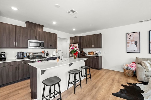 kitchen featuring a breakfast bar area, light countertops, visible vents, appliances with stainless steel finishes, and a kitchen island with sink