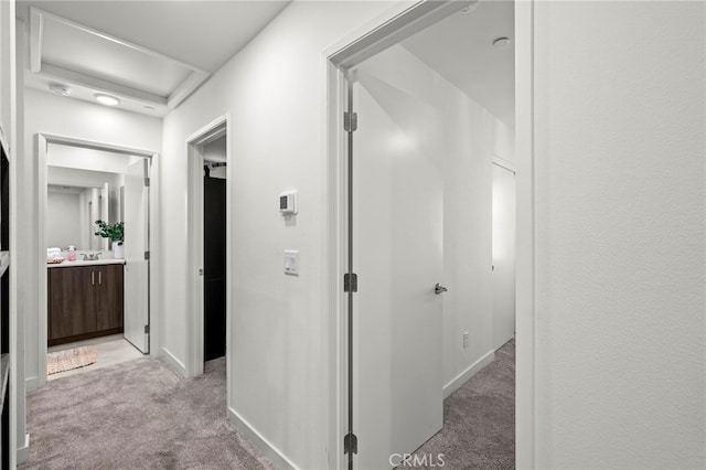 hall with attic access, baseboards, and light colored carpet