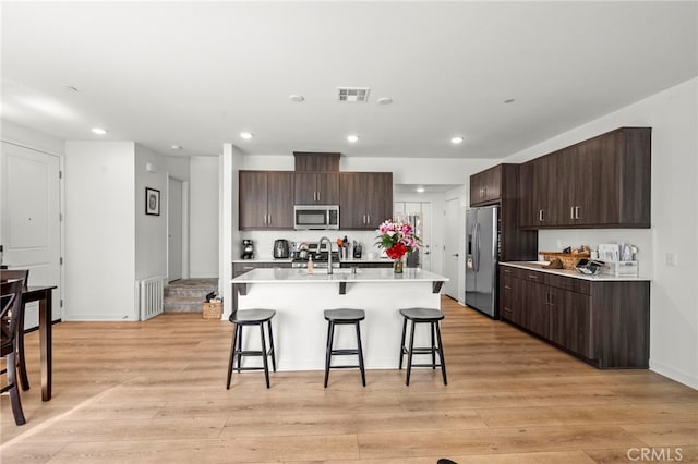 kitchen featuring a breakfast bar area, dark brown cabinetry, stainless steel appliances, light countertops, and an island with sink