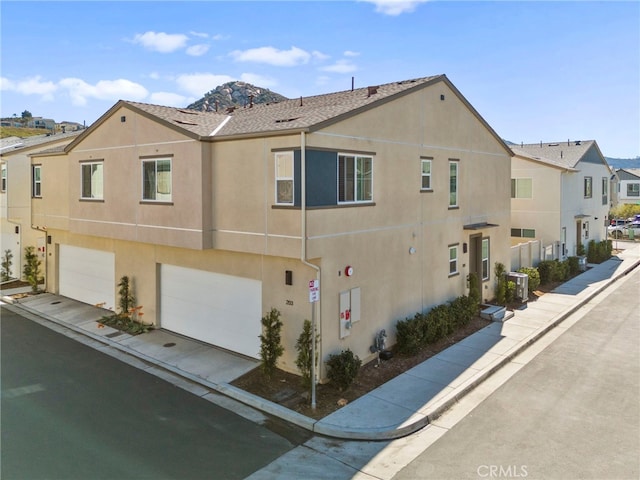 exterior space featuring central AC unit, a garage, driveway, a residential view, and stucco siding