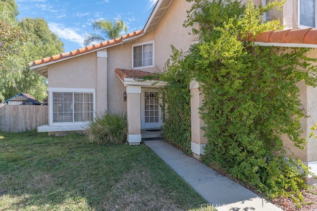 exterior space with a tiled roof, a lawn, fence, and stucco siding