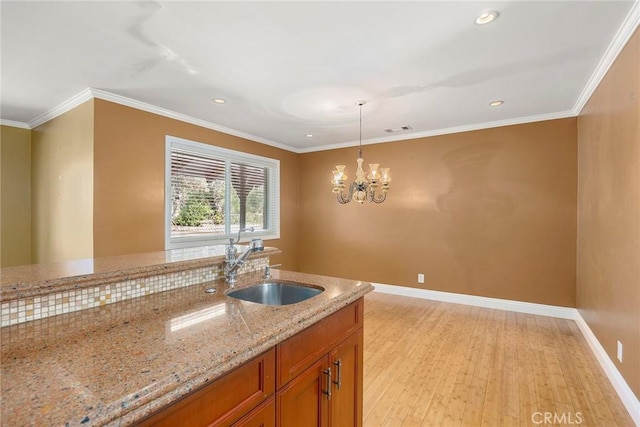 kitchen featuring baseboards, light stone counters, decorative light fixtures, crown molding, and a sink