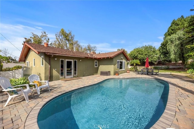 rear view of property featuring stucco siding, fence, an outdoor pool, and a patio