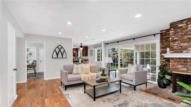 living area with light wood finished floors, baseboards, ceiling fan, a brick fireplace, and recessed lighting