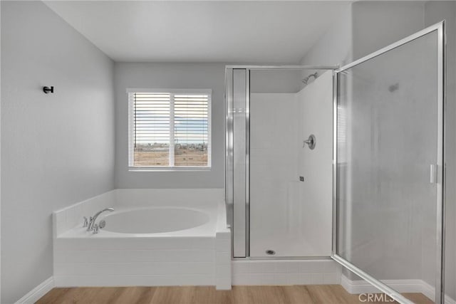 bathroom featuring baseboards, a shower stall, a bath, and wood finished floors