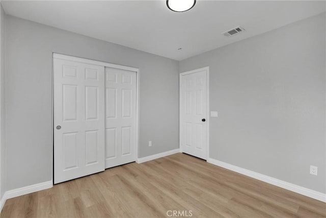 unfurnished bedroom with a closet, light wood-type flooring, visible vents, and baseboards