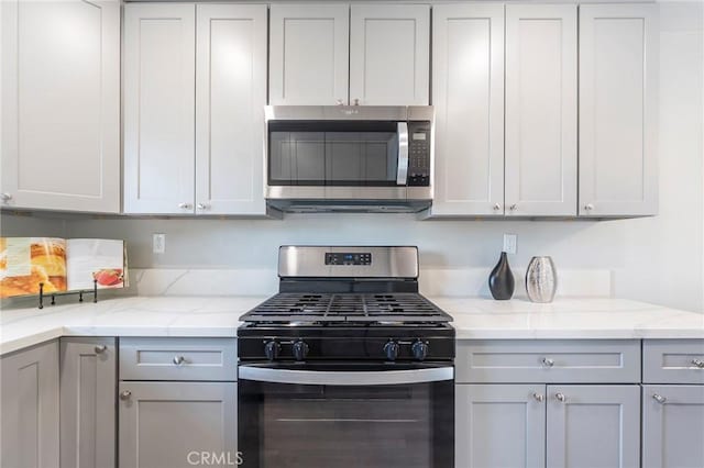 kitchen with stainless steel microwave, light stone countertops, black gas stove, and gray cabinetry