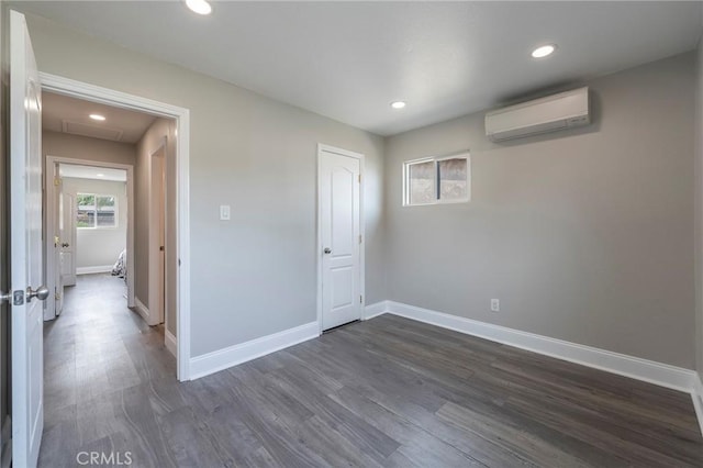 unfurnished bedroom with recessed lighting, dark wood-type flooring, attic access, a wall mounted air conditioner, and baseboards