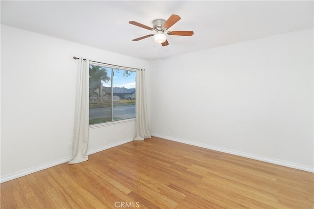 empty room featuring baseboards, a ceiling fan, and light wood-style floors