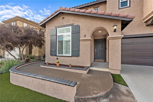 property entrance featuring a garage, a tile roof, and stucco siding