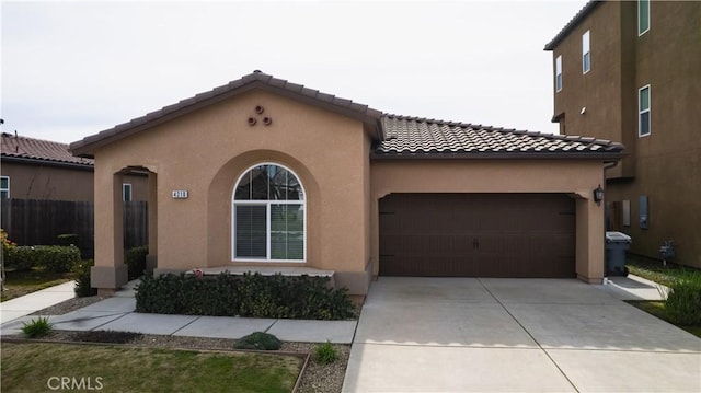 mediterranean / spanish home with concrete driveway, a tile roof, an attached garage, and stucco siding