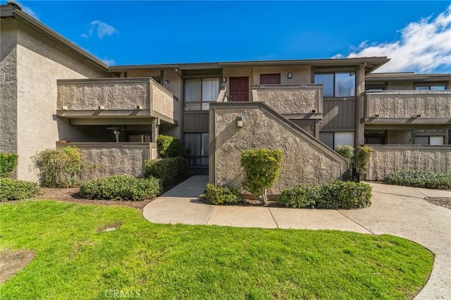 view of front of home featuring a balcony, a front lawn, and stucco siding