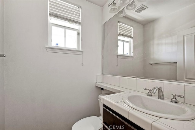 half bath with toilet, backsplash, vanity, and visible vents