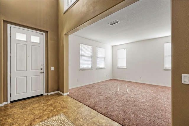 foyer entrance with carpet flooring, visible vents, baseboards, and a textured ceiling