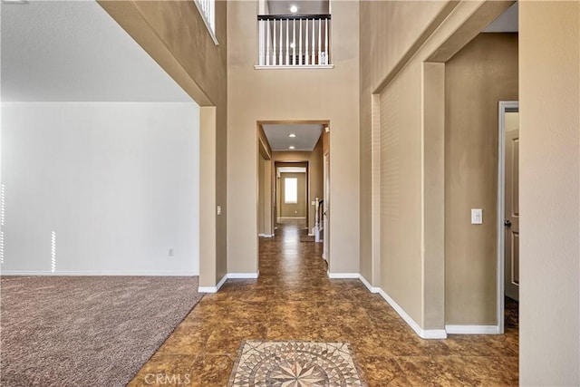 corridor featuring a towering ceiling, baseboards, and dark carpet