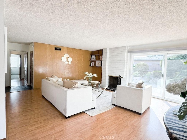 living room featuring a textured ceiling, a brick fireplace, wood finished floors, and visible vents