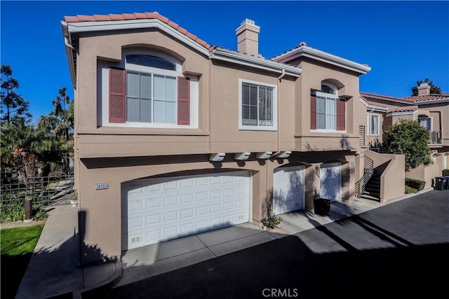 multi unit property featuring a garage, a tile roof, a chimney, and stucco siding