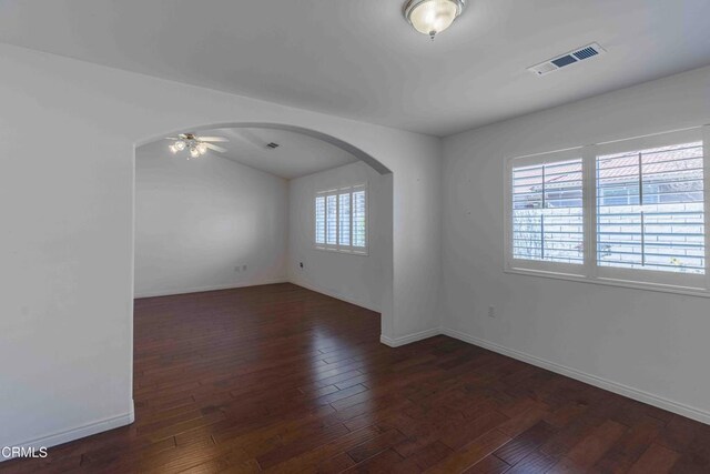 spare room with arched walkways, visible vents, dark wood finished floors, and ceiling fan