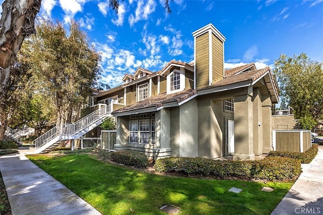 view of front of home featuring a front yard, stucco siding, a chimney, and stairs