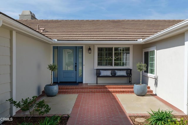 doorway to property with covered porch, a tiled roof, and stucco siding