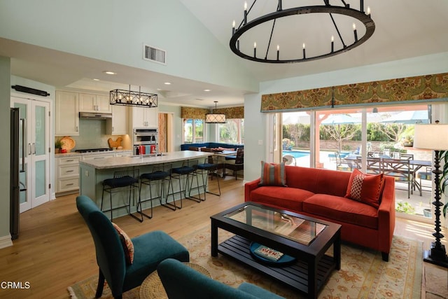 living room featuring high vaulted ceiling, light wood-style flooring, visible vents, and a chandelier