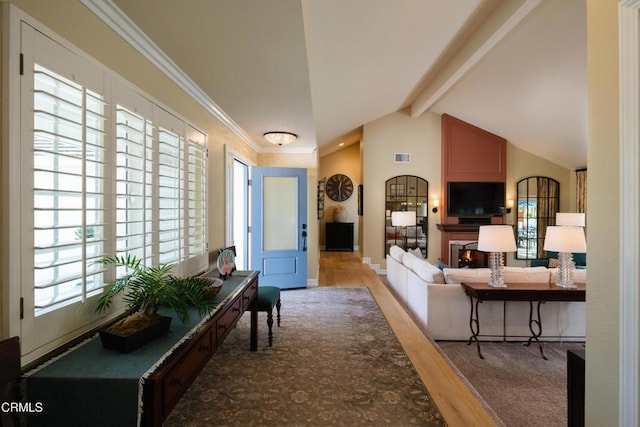 living area with lofted ceiling with beams, light wood finished floors, a fireplace, and a wealth of natural light