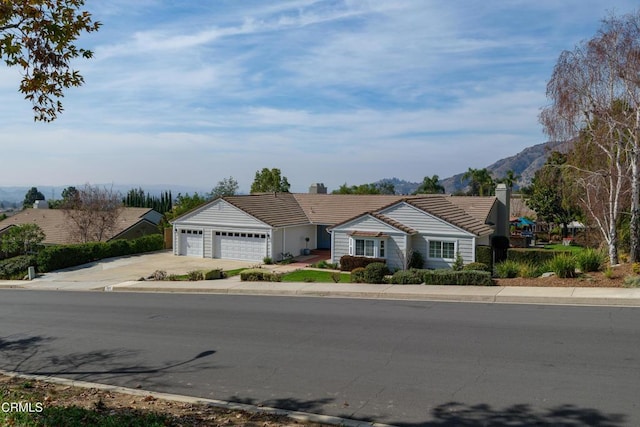 ranch-style house with a garage, a tiled roof, a mountain view, and driveway