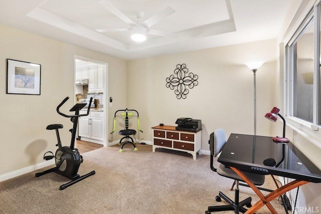 exercise room with baseboards, a tray ceiling, ceiling fan, and light colored carpet