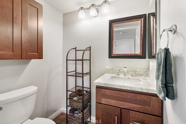 half bath featuring baseboards, vanity, and toilet