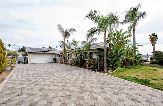 view of front of home with an attached garage, fence, decorative driveway, roof mounted solar panels, and a front yard