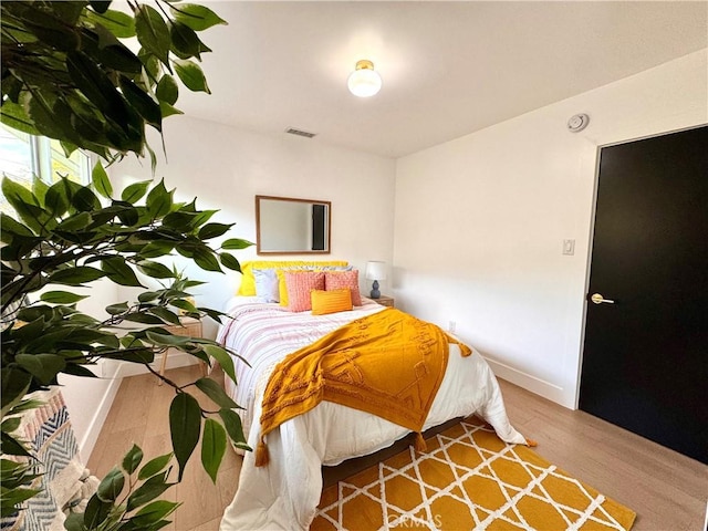 bedroom with wood finished floors, visible vents, and baseboards