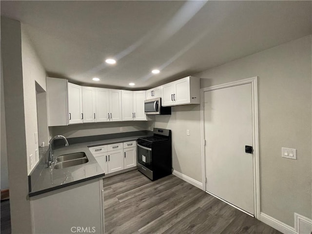 kitchen with dark wood-style flooring, dark countertops, appliances with stainless steel finishes, white cabinets, and a sink