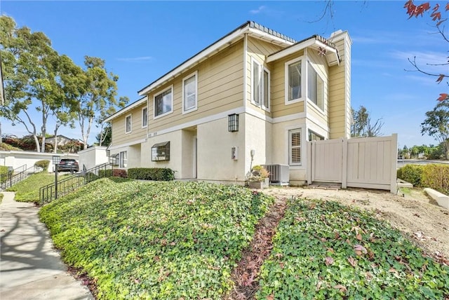 view of property featuring central AC, fence, and stucco siding