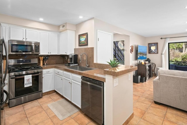 kitchen with tile counters, white cabinets, a peninsula, stainless steel appliances, and a sink