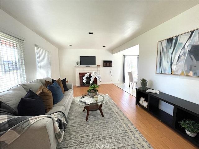 living room featuring a brick fireplace, wood finished floors, and baseboards