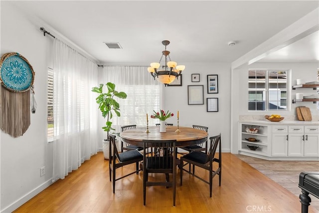 dining space with a chandelier, light wood finished floors, visible vents, and baseboards