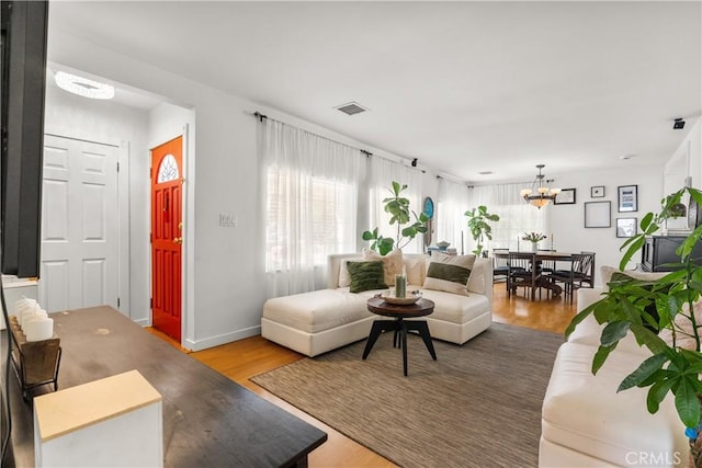 living area featuring an inviting chandelier, wood finished floors, visible vents, and baseboards