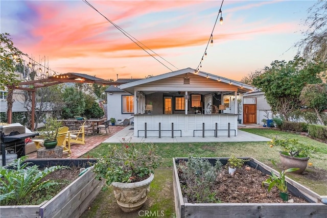 rear view of property featuring outdoor dry bar, a patio, a lawn, and a vegetable garden