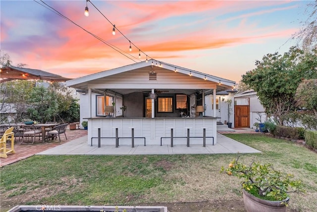 back of house at dusk with a bar, a patio area, and a yard