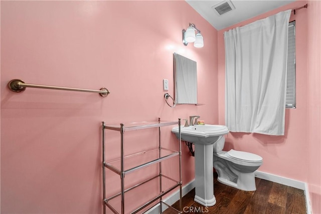 half bath with baseboards, visible vents, toilet, and wood finished floors