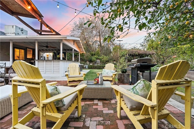 patio terrace at dusk with an outdoor hangout area, an outdoor bar, a ceiling fan, and area for grilling